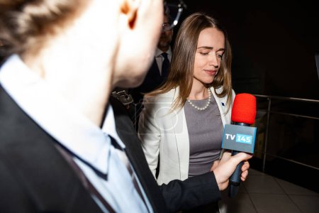 Photo for Positive female EU consul answers press questions and gives interview for media walking in government building corridor. Representative of the European Union surrounded by TV journalists. Press - Royalty Free Image