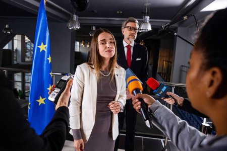 Photo for Political speech of EU consul during press campaign. Confident female European politician answers journalists questions, gives interview for media and television news in European Parliament building. - Royalty Free Image