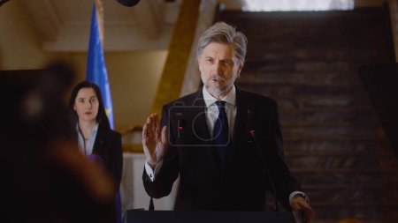 Photo for Mature EU representative comes to press conference and gives interview for social media or TV news in government building hall. Confident consul political speech. Election coverage. Campaign speech. - Royalty Free Image