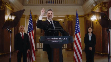Photo for Positive American republican politician poses on cameras for media and television during press conference. US President or congressman smiles and gestures after political speech in the White House. - Royalty Free Image