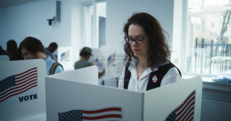Une femme à lunettes vote dans un bureau de vote. Journée nationale des élections aux États-Unis. Courses politiques des candidats à la présidence américaine. Devoir civique et patriotisme. Au ralenti. Dolly shot.