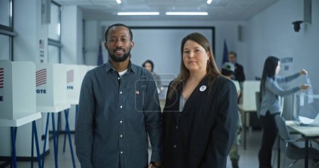 Photo for Portrait of multi ethnic couple, United States of America elections voters. Family stand in a modern polling station, pose, smile and look at camera. Background with voting booths. Civic duty concept. - Royalty Free Image