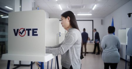 Téléchargez les photos : Angle élevé de personnes européennes multiethniques votant dans les bureaux de vote lors des élections européennes. Divers électeurs remplissent les bulletins de vote dans les isoloirs. Le jour des élections dans l'Union européenne. Devoir civique et démocratie. - en image libre de droit