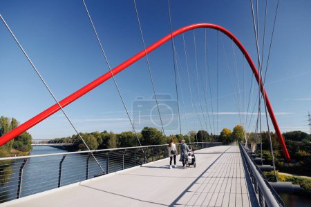 Foto de Puente rojo sobre el río en el Parque Nordstern con mujeres con un cochecito, Schurenbachhalde cerca de Essen, Alemania. - Imagen libre de derechos