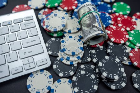 Pokerchips für Poker mit verdrehten Banknoten auf der Laptop-Tastatur platziert. isoliert auf schwarzem Hintergrund. Poker-Konzept