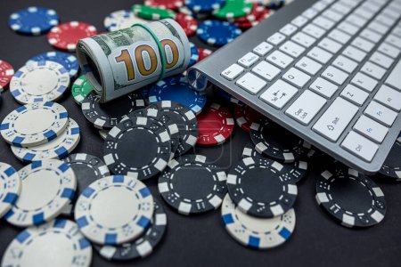 Pokerchips und jede Menge Dollars auf einer Laptop-Tastatur, die über einen einfachen Hintergrund verstreut ist. Glücksspiel. Illegales Pokerspiel