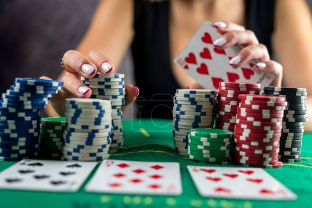 Téléchargez les photos : Une belle femme dans une robe noire du soir joue au poker dans un casino, enveloppant tous les gains dans ses mains. Prend un pari sur tous les jetons. gagner. all-in - en image libre de droit