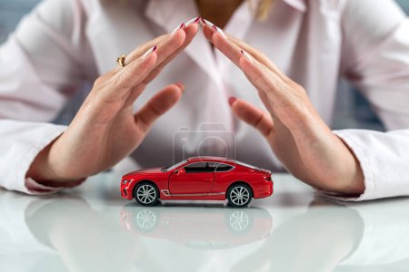 Photo for Beautiful small car in the hands of a woman at the table. Concept of safe driving. protection of life behind the wheel. - Royalty Free Image