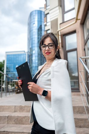 Foto de Portrait of a business woman with chic hair and great makeup standing near a high-rise building. Business style concept. A woman who works in the office - Imagen libre de derechos