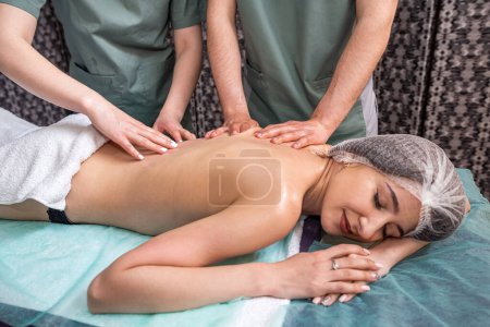 Photo for Back massage in four hands at the same time - two professional massage therapists deal with a female patient. spa salon. skin healing. muscle tone - Royalty Free Image