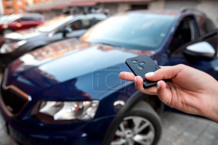 Photo for Hand presses the car alarm control panel in front of his own new car. Reliable vehicle alarm. A hand with a car lock remote control - Royalty Free Image