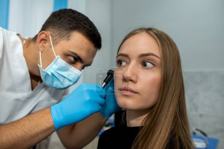 Photo for ENT doctor uses an otoscope to examine a patient's ear during a medical examination at the hospital. A female otolaryngologist consults in her office. - Royalty Free Image