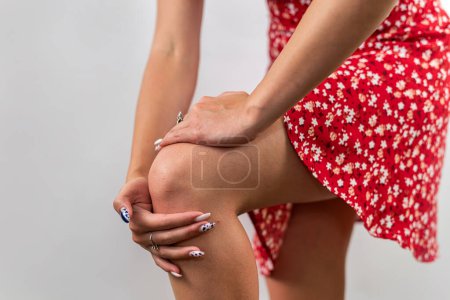 Foto de Mujer con una lesión en la rodilla se dobla y sostiene una mano aislada sobre un fondo blanco. una rodilla femenina dolorida. concepto de salud - Imagen libre de derechos