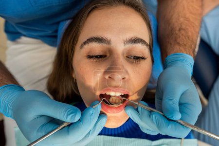 Photo for Dentists with mirror, drill and dental air water gun spray treating adult patient teeth at dental clinic - Royalty Free Image