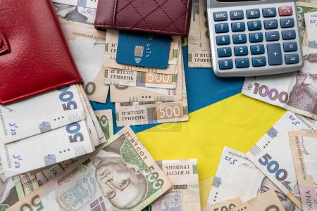 Foto de Ukraine national flag with UAH paper money in wallet, credit card calculator, finance concept, wealthy - Imagen libre de derechos