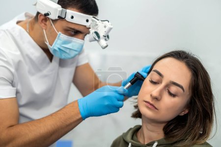 Téléchargez les photos : Examen avancé de l'oreille d'une femme à l'aide d'un otoscope lors d'un rendez-vous chez le médecin. Otoscopie. Visite au médecin ORL et consultation - en image libre de droit