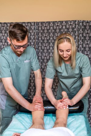 Photo for Two massage therapists a woman and a man give a four-handed anti-cellulite leg massage to a female client in a spa salon. massage in four hands. spa treatments - Royalty Free Image