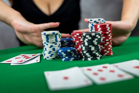 Téléchargez les photos : Une belle femme dans une robe noire du soir joue au poker dans un casino, enveloppant tous les gains dans ses mains. Prend un pari sur tous les jetons. gagner. all-in - en image libre de droit