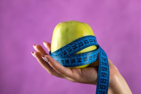 Téléchargez les photos : Femme qui veut perdre du poids avec une pomme et un ruban à mesurer isolé sur un fond blanc. concept de santé - en image libre de droit
