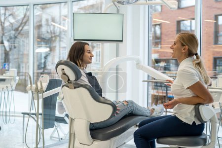 Téléchargez les photos : Une dentiste et une cliente discutent lors d'une consultation dans une clinique dentaire. Discussion des questions. Soins médicaux et dentaires. Nomination professionnelle - en image libre de droit