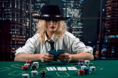 attractive girl in shirt and hat covering face with hat holding poker cards in casino. poker. lady player