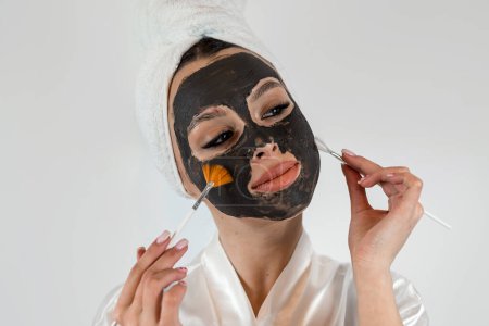 Téléchargez les photos : Portrait de belle femme faisant des traitements de beauté utilisent masque d'argile et tenir le pinceau isolé sur blanc. Concept de beauté et de santé, traitement anti-âge - en image libre de droit