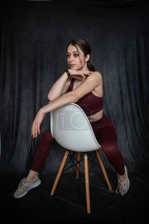 Photo for Sporty young woman wear sport cloth near chair isolated on black. Portrait of pretty woman - Royalty Free Image