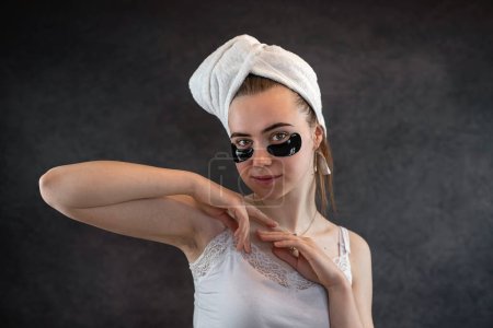 Photo for Young cute girl in white towel clean skin with black silicone patches isolated on black background. Patches for skin care dark circles under eyes - Royalty Free Image