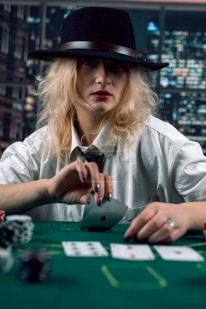 Photo for Attractive girl in shirt and hat playing poker and holding cards in casino. woman player.poker. excitement - Royalty Free Image