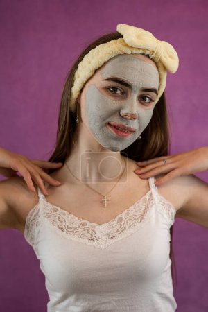 Foto de Hermosa mujer con mascarilla facial de arcilla verde terapéutica aislada en púrpura. Tratamiento anti envejecimiento Spa - Imagen libre de derechos