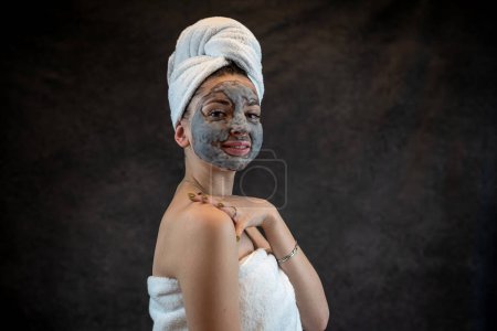 Beautiful young woman wear white towel applying gray oxygen bubbling mask isolated on black, anti aging treatment, perfect skin