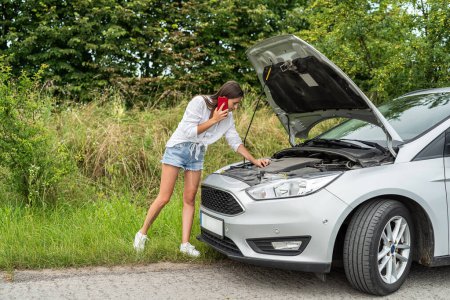 Téléchargez les photos : Femme conducteur regardant sous le capot de la voiture, cassé auto pendant le voyage. Compartiment moteur d'une voiture en panne - en image libre de droit