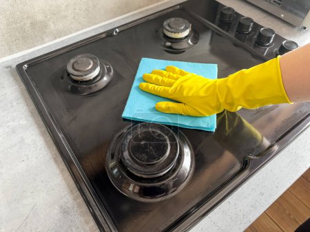 famale Hand in gelben Handschuhen wischt den Küchenherd mit trockenem Schwamm ab. Hausreinigung