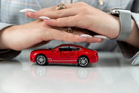 Nahaufnahme weiblicher Hände mit rotem Spielzeugauto als Versicherungsschutzkonzept. Garantiegarantie