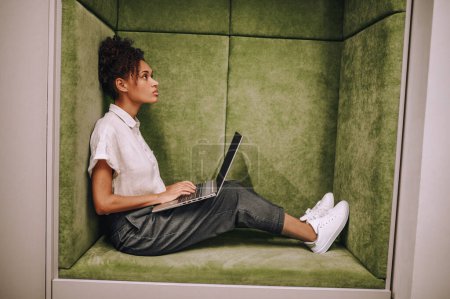 Photo for Side view of a serious beautiful female with her laptop sitting in the introvert workplace - Royalty Free Image