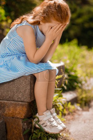 Upset. A kid in a blue dress sitting and looking upset