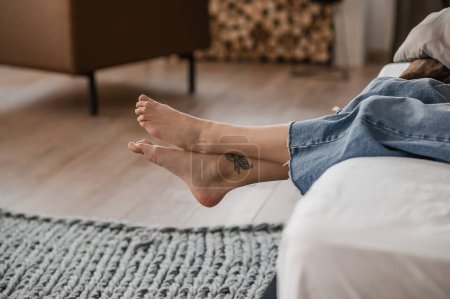 Foto de Cropped photo of a barefoot female person dressed in trendy jeans lying on the bed - Imagen libre de derechos