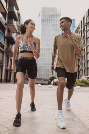 Photo for Full-length portrait of a smiling sporty girl and a cheerful fit guy doing power walking - Royalty Free Image