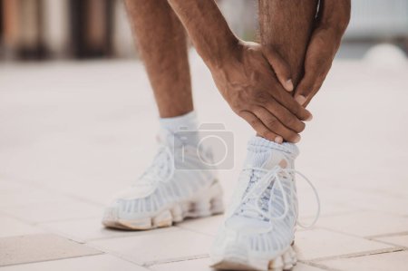 Foto de Cropped photo of an African American male runner touching his painful ankle after the workout - Imagen libre de derechos