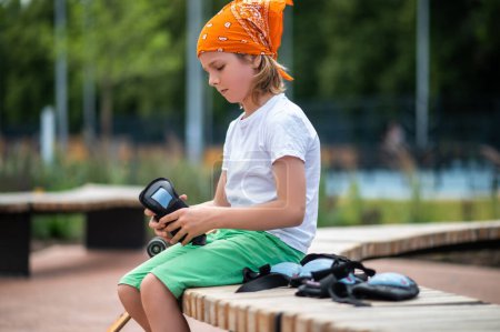 Photo for Serious focused cute boy sitting on the bench and looking at wrist guards in his hands - Royalty Free Image
