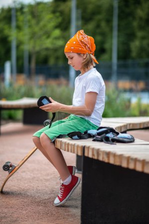 Photo for Serious concentrated preteen child seated on the wooden bench holding the wrist guards in his hands - Royalty Free Image