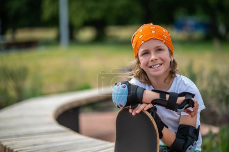 Photo for Smiling happy preteen boy in the wrist guards and elbow pads leaning on his skateboard - Royalty Free Image