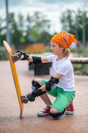 Photo for Focused calm young skateboarder sitting on his haunches and checking the wheels of his skateboard - Royalty Free Image