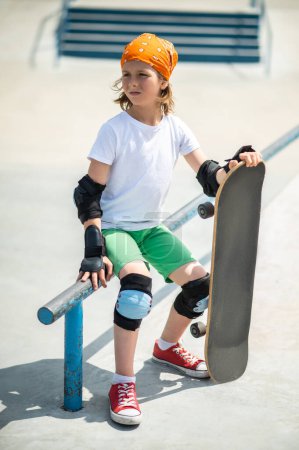 Photo for Serious focused preteen child with the skateboard seated on the guardrail staring into the distance - Royalty Free Image