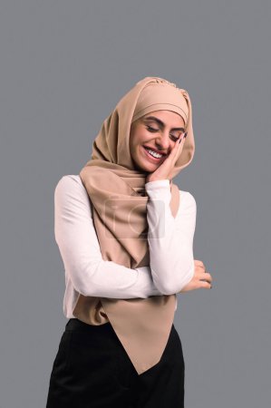 Téléchargez les photos : Une femme heureuse. Arabe jeune femme en hijab beige regardant heureux et satisfait - en image libre de droit