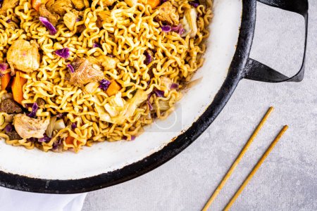 Photo for Japanese yakisoba with stir-fried noodles in white metallic pan on table with white tablecloth and black background, with chopsticks of Japanese food.. Close view. - Royalty Free Image