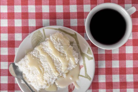Photo for Piece of couscous in porcelain saucer on checkered tablecloth, typical Brazilian dish, made with tapioca, milk, sugar and coconut milk. With cup of coffee. Top view. - Royalty Free Image