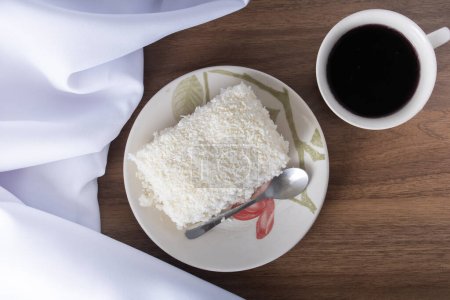 Photo for Piece of couscous in porcelain saucer on wooden table, typical Brazilian dish, made with tapioca, milk, sugar and coconut milk. With coffee cup. Perspective view. - Royalty Free Image