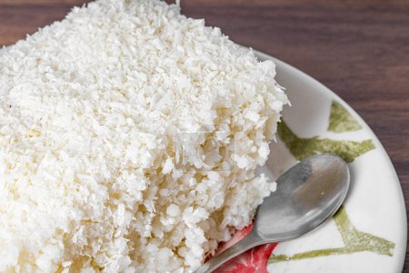 Photo for Piece of couscous in porcelain saucer on wooden table, typical Brazilian dish, made with tapioca, milk, sugar and coconut milk. Close view. - Royalty Free Image