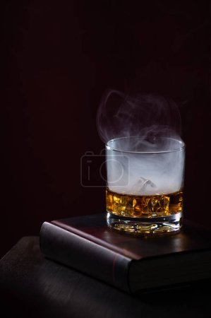 Téléchargez les photos : Liqueur d'orange et de pêche avec un effet fumée blanche sur un livre noir avec du rouge, cocktail du soir, personne - en image libre de droit